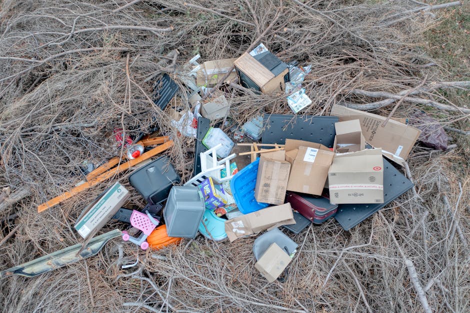 The image depicts an open, dry landfill site with several small tractors and trailers, some filled with mixed waste materials including textiles, plastics, and household trash. The vehicles are positi